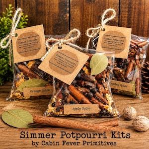 May include: Three clear plastic bags filled with simmer potpourri, each featuring a brown paper tag tied with twine. The tags are labelled Simmer Potpourri, Orange Spice, Apple Spice, and Country Spice. The bags contain cinnamon sticks and leaves.