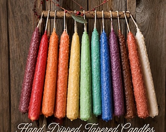 May include: A collection of twelve hand-dipped tapered candles in a spectrum of colors including burgundy, red, orange, yellow, green, blue, purple, brown, and white, hanging from a wooden rod with the text Hand Dipped Tapered Candles by Cabin Fever Primitives.