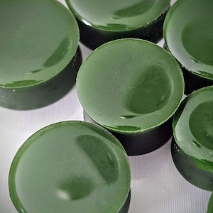 May include: A group of eight round, green, shiny, smooth, disc-shaped objects. The objects are arranged in a semi-circle on a white surface.