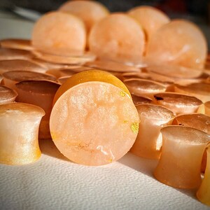 May include: A close-up of a set of peach-colored ear gauges with gold flecks. The gauges are made of resin and have a smooth, polished finish.