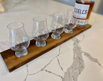 May include: A wooden serving tray with four small glasses and a bottle of Russell's Reserve bourbon whiskey. The tray is made of dark wood and has a natural finish.