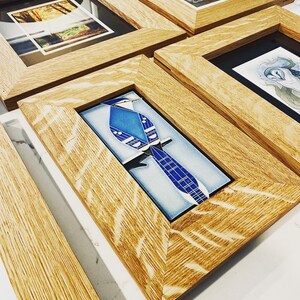 May include: Four wooden picture frames with different images inside. The frames are all made of a light brown wood with a natural grain. The images inside the frames are a forest scene, a blue bird, a floral design, and a bird on a branch.