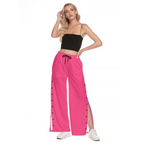 May include: Pink wide-leg pants with a drawstring waist and button detailing on the sides. The pants have a white stripe down the side seams.