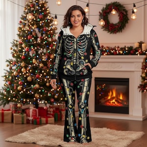 May include: A black skeleton-themed zip-up hoodie and matching flared trousers. The skeleton design is overlaid with colourful Christmas lights. The hoodie has a white, fluffy-lined hood. The outfit is worn in front of a decorated Christmas tree and fireplace.