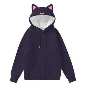 Op de afbeelding: Een donkerpaarse hoodie met kattenoren op de capuchon. De binnenkant van de capuchon is wit, met roze accenten. Een gele halve maan is ook aanwezig. De hoodie heeft een voorzak en zwarte trekkoorden.