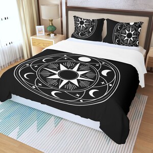 May include: Black and white bedding set with a celestial design featuring a sun, moon, and stars. The design is in a circle with a white outline.