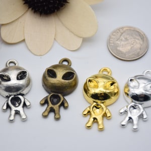 May include: Four silver and gold alien charm pendants. The charms are in the shape of an alien with large eyes and a small body. The charms are perfect for adding a fun and quirky touch to jewelry.