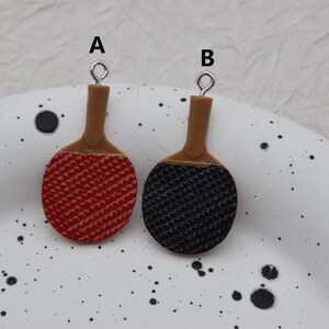 May include: Two miniature ping pong paddles with brown handles. One paddle has a red surface and the other has a black surface.