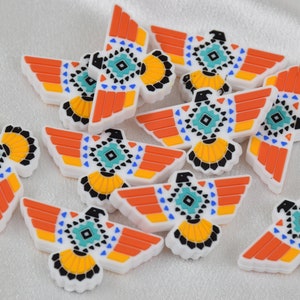 Op de afbeelding: Een verzameling van 10 witte, oranje, gele, blauwe en zwarte adelaar bedels met geometrische patronen. De bedels zijn gemaakt van siliconen en zijn perfect om een ​​touch van Native American stijl toe te voegen aan je sieraden of knutselwerk.