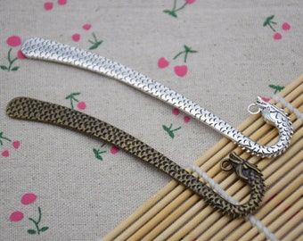 May include: Two silver dragon bookmark pendants. One is silver and the other is bronze. Both have a textured, scaly design.