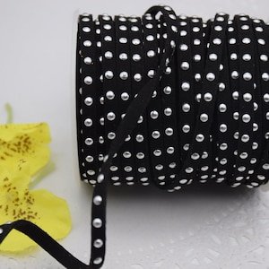 Puede incluir: Un carrete de cordón de ante negro con puntos plateados. El cordón está enrollado alrededor de un carrete blanco.