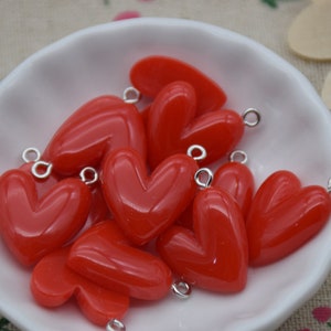 Puede incluir: Un bol de abalorios rojos en forma de corazón con anillas de salto plateadas. Los abalorios están hechos de un material brillante y liso.