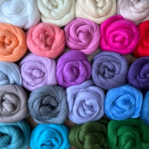 May include: A collection of 18 colorful balls of wool fiber, arranged in a circular pattern. The colors include white, pink, purple, blue, green, and gray.