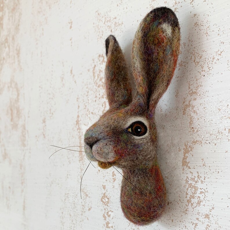 Puede incluir: Una escultura de fieltro marr&oacute;n y gris de la cabeza de una liebre con una nariz larga y ojos grandes y oscuros.