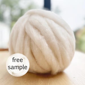 May include: A large, off-white ball of wool roving. The wool has a soft, textured appearance. A white circle with the words "free sample" is in the foreground. The wool is likely for crafting projects like arm knitting or felting.