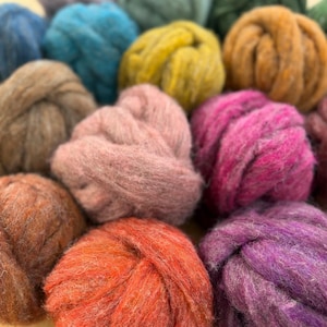 May include: A collection of thick, textured yarn balls in various colors including bright orange, soft pink, deep magenta, mustard yellow, brown, and teal. Each ball is composed of loosely spun, fuzzy fibers with a visible, chunky weave.