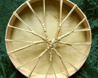 May include: A round, wooden frame drum with a natural leather head. The drum is laced with a woven pattern of natural fibres.