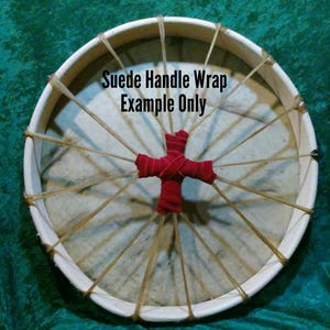 Pode incluir: Tambor branco com uma envoltura de al&ccedil;a de camur&ccedil;a vermelha. O tambor &eacute; feito de madeira e tem uma cabe&ccedil;a de couro. A envoltura da al&ccedil;a &eacute; amarrada em forma de cruz. "Suede Handle Wrap Example Only" est&aacute; escrito no tambor.