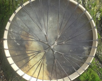 May include: A large, round, wooden frame drum with a dark brown leather head. The drum is strung with black leather lacing, creating a starburst pattern in the centre.