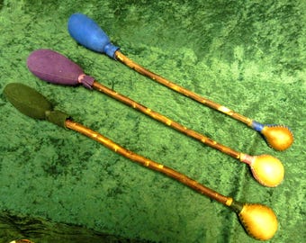 May include: Three wooden sticks with leather-covered ends. The ends are different colors: blue, purple, and green. The sticks are on a green background.