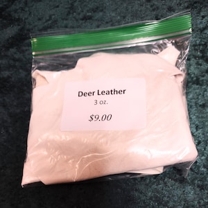 May include: A clear plastic bag with a green zipper contains pieces of white deer leather. A white label on the bag reads "Deer Leather" and "3 oz."