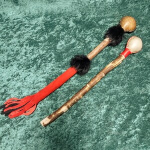 May include: Two wooden shakers with leather and fur accents. One shaker has a red and black tassel, the other has a black fur pom-pom.