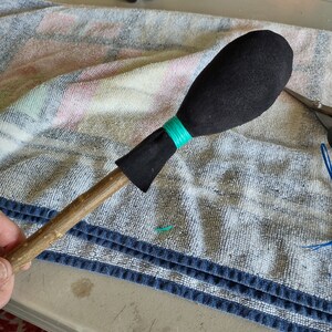 May include: A wooden stick with a black fabric ball on the end. The ball is secured with a turquoise string.