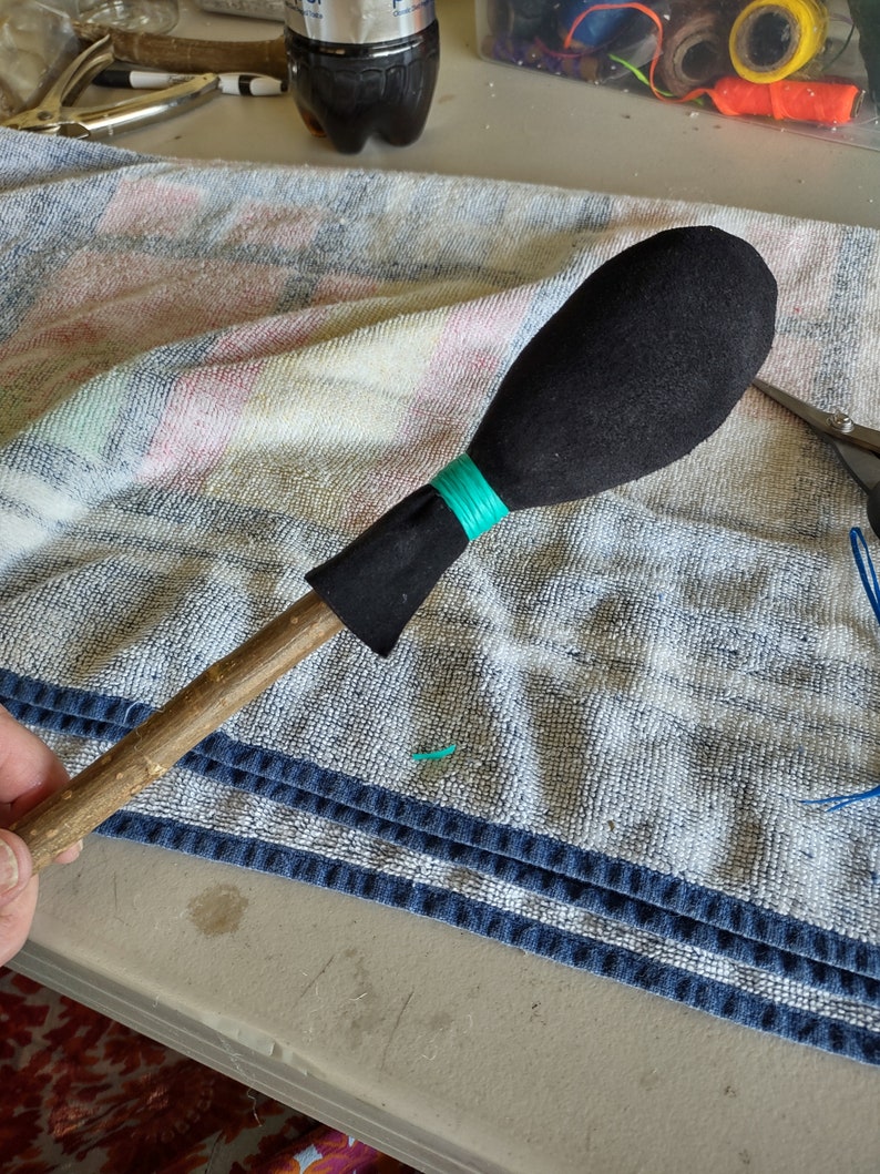 May include: A wooden stick with a black fabric ball on the end. The ball is secured with a turquoise string.