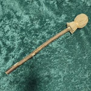 May include: A percussion mallet featuring a long, straight wooden handle with a natural bark texture and a rounded, beige fabric-covered head secured with a light-colored band at the base, creating a functional tool for musical instruments.
