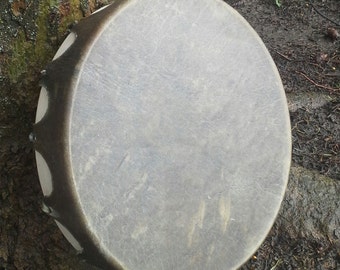 May include: A round, light brown leather drum with a dark brown wooden frame and metal tuning lugs.