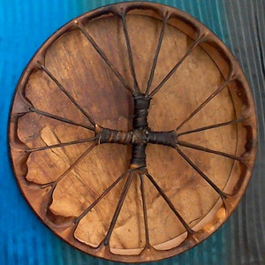Pode incluir: Um tambor de moldura de madeira marrom com uma cabe&ccedil;a de couro e um padr&atilde;o de renda preto. O tambor &eacute; feito de materiais naturais e tem um aspecto r&uacute;stico.