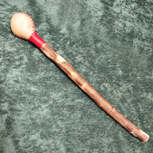 May include: A wooden stick with a leather-covered head, used for playing a musical instrument. The head is white with red stitching and the stick is brown with a natural finish.