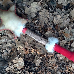 May include: A whimsical star-shaped wand with a cream-colored center and red stitched edges. The wand features a wooden handle, red fabric accents, and white fluffy trim. The wand is designed to look like a star and is a toy.