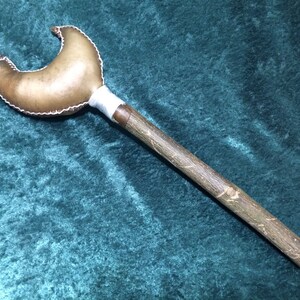 May include: A brown leather rattle with a wooden handle. The leather is stitched together and has a crescent moon shape. The handle is about 12 inches long.