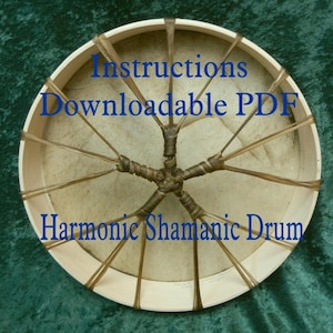 Può includere: Primo piano di un tamburo a cornice di legno con una pelle in cuoio marrone chiaro. Il tamburo è legato con cinghie in cuoio marrone e ha il testo "Instructions Downloadable PDF Harmonic Shamanic Drum" stampato su di esso.