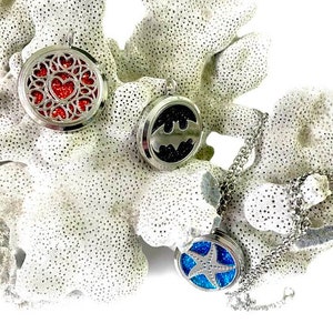 May include: Three silver essential oil diffuser necklaces with different designs. One has a red glitter heart, one has a black glitter Batman logo, and one has a blue glitter starfish.
