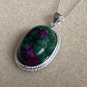May include: A silver chain necklace with a green and pink oval pendant. The pendant is set in a silver bezel with a rope-like edge.