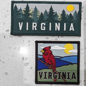 May include: Two embroidered patches with the word "VIRGINIA" in white text on a green background. The top patch features a forest scene with a yellow sun. The bottom patch features a red cardinal bird perched on a branch with a blue sky and mountains in the background.