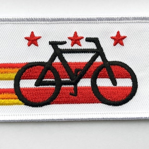 May include: White embroidered patch with a black bicycle silhouette on top of three red and yellow stripes. Three red stars are above the bicycle.