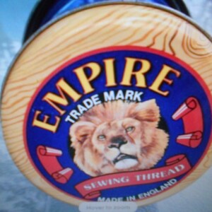 May include: A spool of Empire sewing thread. The label features a lion's head in the center, surrounded by the words "EMPIRE TRADE MARK SEWING THREAD MADE IN ENGLAND" in a blue and red design.
