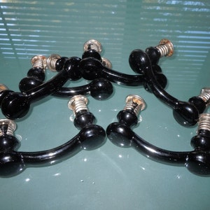 May include: Six black glass cabinet knobs with silver metal bases. The knobs are shaped like a rounded arch with a rounded end on each side.