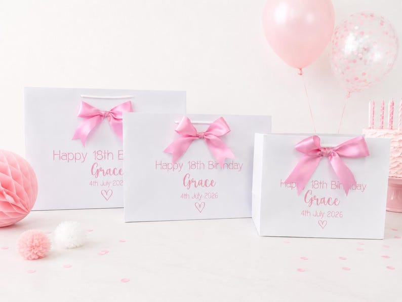 Puede incluir: Tres bolsas de regalo blancas con lazos rosas, personalizadas con "Happy 18th Birthday Grace" y la fecha. Una bola de panal rosa, globos y confeti completan la escena festiva. Las bolsas son de diferentes tama&ntilde;os.