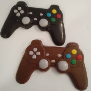 May include: Two chocolate game controllers, one brown and one black, with white buttons and colorful face buttons.