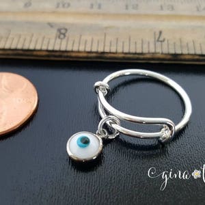 K&ouml;nnte beinhalten: Ein verstellbarer Silberring mit einem Anh&auml;nger in Form eines blauen und wei&szlig;en b&ouml;sen Auges. Der Ring liegt neben einem Centst&uuml;ck zum Gr&ouml;&szlig;envergleich.