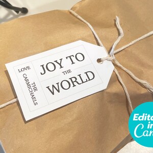 Puede incluir: Un paquete de papel marrón atado con cuerda y una etiqueta de regalo blanca que dice "JOY TO THE WORLD" y "LOVE THE CARMICHAELS".