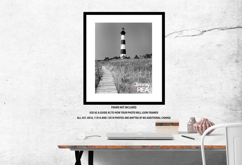 May include: Black and white framed print of a lighthouse with a black and white striped tower, standing tall amidst tall grass. A wooden walkway leads to the lighthouse. The text "Jimmy REA" is visible.
