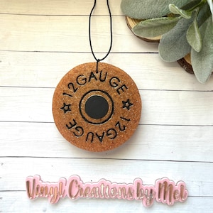 May include: A brown wooden round ornament with a black circle in the center and the text "12 GAUGE" around the circle. The ornament is hanging from a black string.