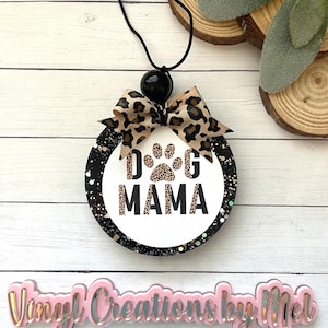 May include: A round, black and white air freshener with the text "DOG MAMA" and a paw print design. It features a leopard print bow and a black string for hanging. The product is designed for pet lovers.