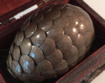 May include: A dragon egg replica made of metal with a scaly texture, displayed in a wooden box with a hinged lid and a metal latch.