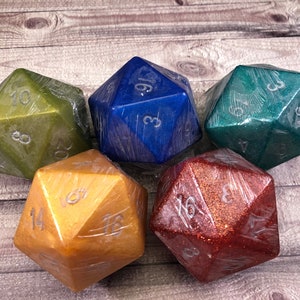 May include: Five iridescent, glittery, multi-sided dice in various colors: green, blue, teal, gold, and red. The dice are all in focus and are arranged in a circle on a wooden surface.